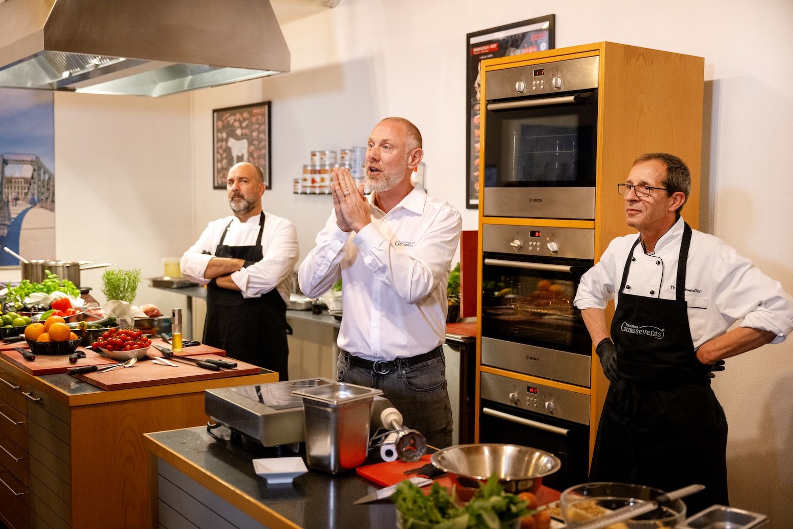 Mehrere Köche und Kursleiter stehen in einer modernen Kochschule in Frankfurt und begrüßen die Teilnehmenden eines Genussevents, vor ihnen liegen frische Zutaten und Küchenutensilien bereit.